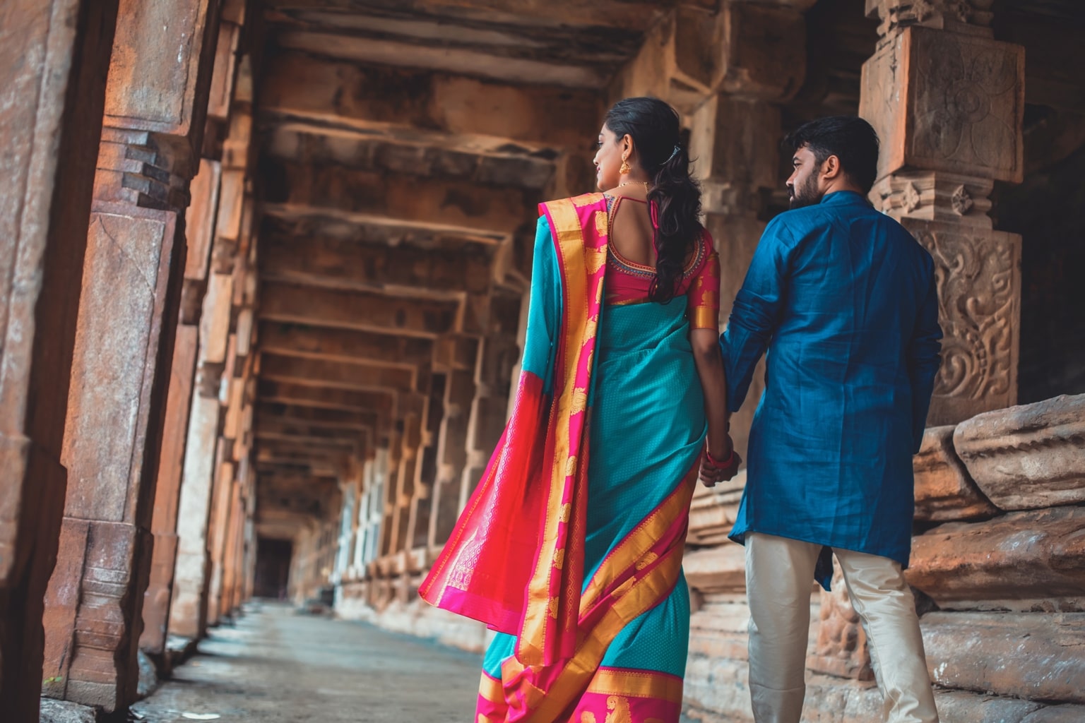 candid pre wedding picture of bride and groom holding hands and walking in a temple